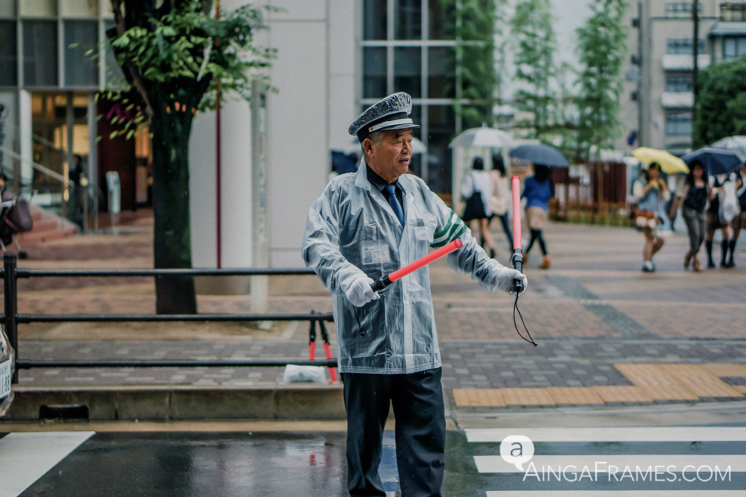 A crossing guard directing traffic in front of a giant shopping center in Kyoto on a cold, rainy day.